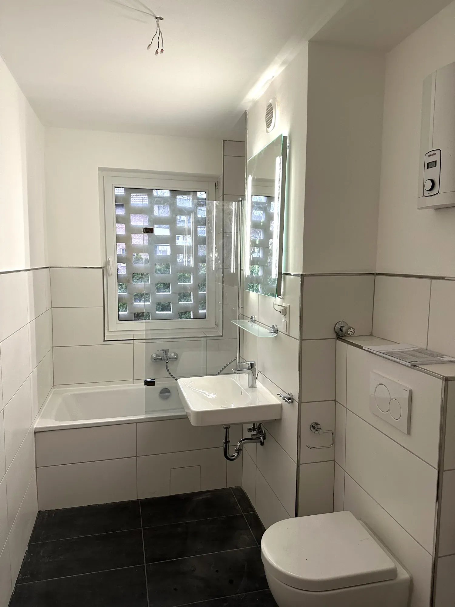 Saniertes Badezimmer mit Badewanne, wandhängendem Waschtisch, WC und beleuchtetem Spiegel