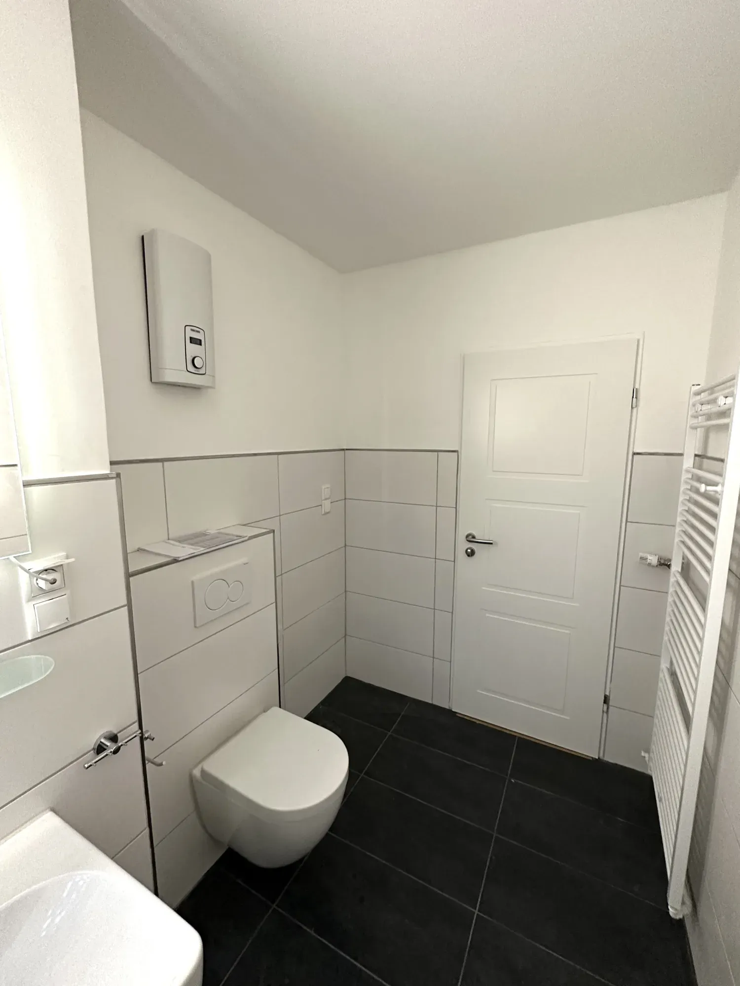 Blick im Bad auf WC mit Vorwandinstallation, Handtuchheizkörper und neue Innentür