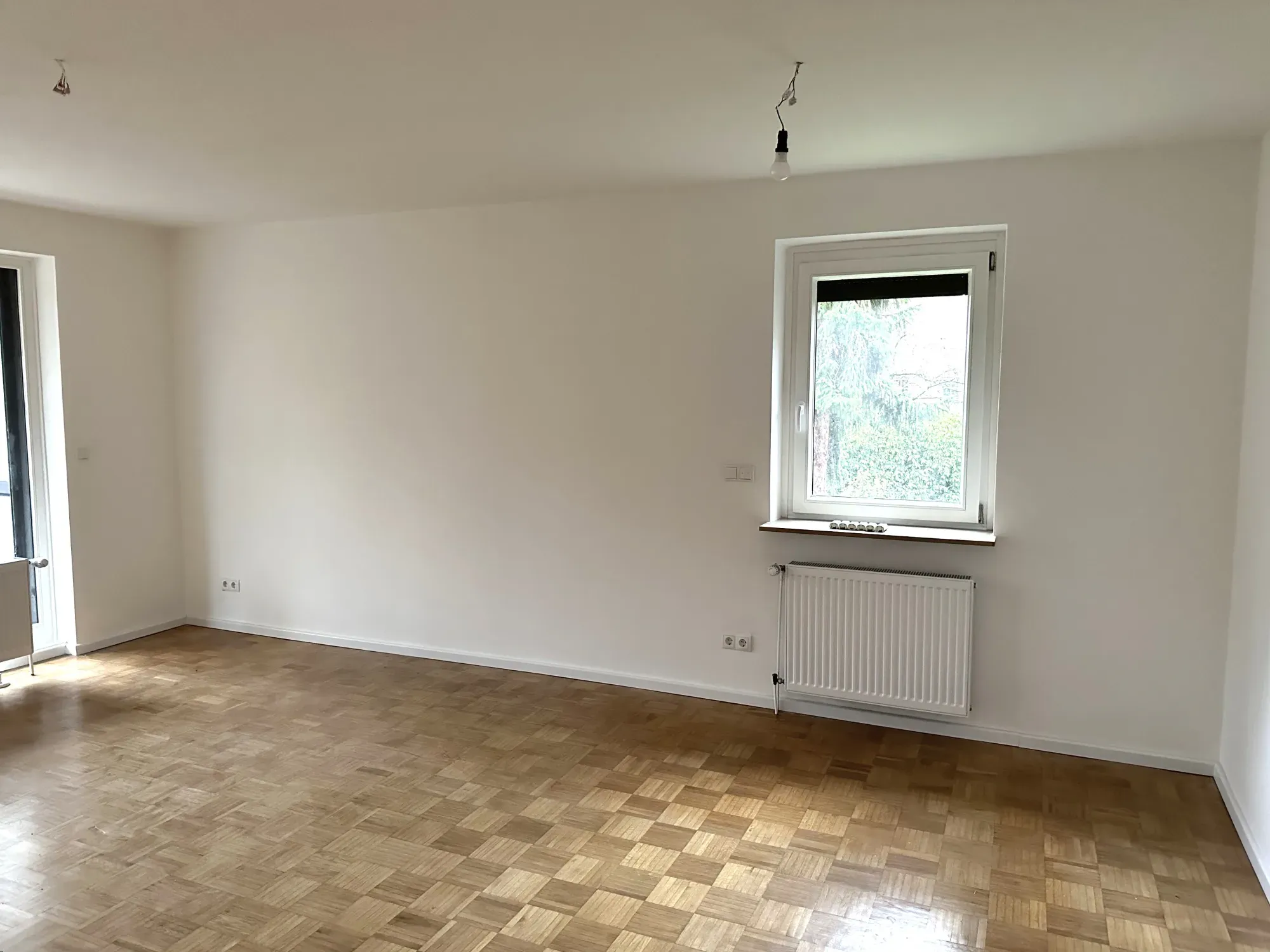 Leerer heller Wohnraum mit frisch gestrichenen Wänden, Parkettboden und neuem Heizkörper unter dem Fenster